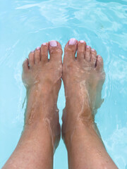 A pair of female feet with neatly pedicured toenails painted in soft pink, submerged in clear light...