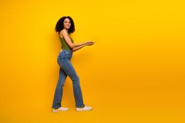Stylish young woman in a green top and jeans posing against a vibrant yellow background, radiating confidence and joy