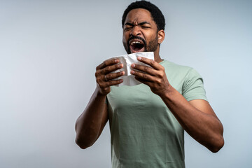 Handsome African-American man sneezing into tissue, suffering from cold or allergy, isolated on...