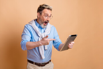 Mature gentleman with tablet expressing surprise while wearing casual yet elegant attire on beige...