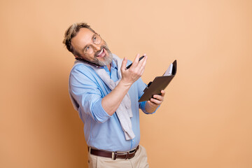 Confident mature businessman multitasking with phone and organizer against beige background in...