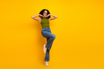 Stylish young woman with black curly hair posing in casual green top and jeans against a vibrant...