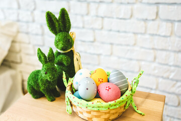 Colorful Easter eggs in a basket with decorative bunnies on a wooden table