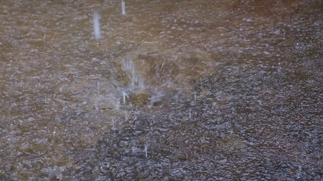A puddle of water with raindrops falling on it. The water is murky and the rain is coming down in a steady stream