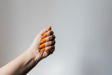 Hand with bright orange nails holds a fist against a plain white background