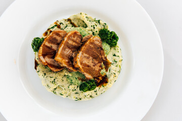 Grilled chicken slices served on a bed of spinach mashed potatoes with garnished broccoli