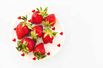 Fresh strawberries arranged on a white plate with red heart decorations for occasions