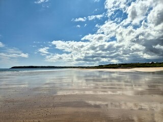 Sandy beach and cliffs on Rocky Irish coast - Wild Atlantic Way, Ireland - reflection of clouds in water on sand