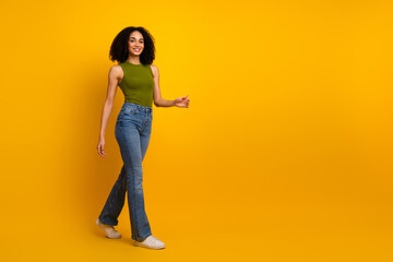 Young fashionable woman walking confidently in casual green top and jeans, showcasing vibrant style against yellow background