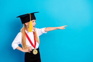 Joyful schoolgirl in graduation attire pointing ahead wearing a medal, expressing achievement and...