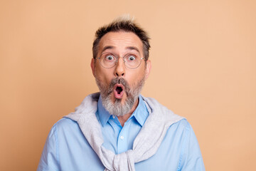 Surprised mature gentleman in casual attire expressing astonishment against beige background for...