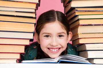Smiling child with braided hair studying surrounded by colorful book on a pink background, evoking...