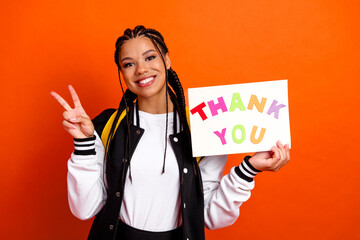 Happy student holding thank you sign in colorful letters, flashing peace gesture on bright orange...