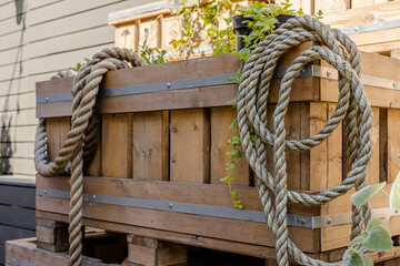 Rustic wooden planter box with coiled rope and sprouting plants. Outdoor gardening idea, nautical...