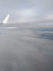 View from an airplane window showing the aircraft wing flying high above thick, soft clouds under a...