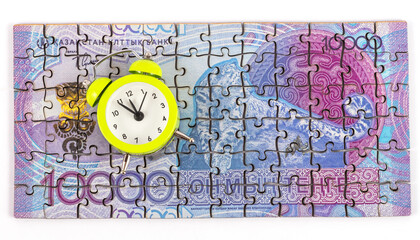 A 10,000 Kazakhstani tenge banknote made from puzzles and an alarm clock on a white background