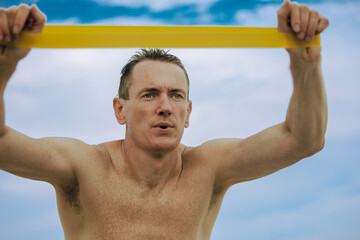 Adult male with freckles on his body working out with a fitness resistance band outside on the...