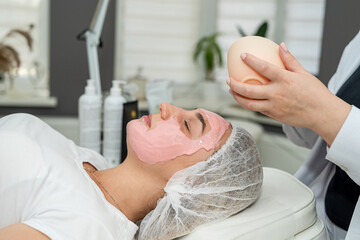 Young woman lying in spa and relax with with pink facial mask