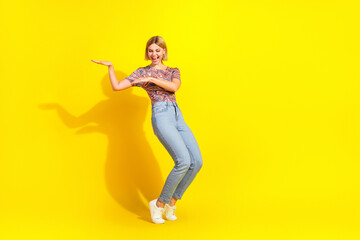 Cheerful young woman in casual trendy outfit posing vibrantly against bright yellow background,...