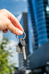 Keys to Success: Hand Holding Keys Against Futuristic Skyscraper. Symbolic image of a hand holding a bunch of keys with a modern glass skyscraper