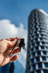 Keys to Success: Hand Holding Keys Against Futuristic Skyscraper. Symbolic image of a hand holding a bunch of keys with a modern glass skyscraper