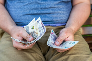 Counting Polish Zloty – Hands of a Man with Wallet and Cash.  A man in casual clothes holding and counting Polish zloty notes from a black leather wallet.