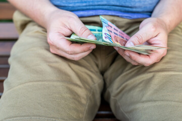 Counting Euro Cash – Man Holding Wallet and Banknotes Outdoors. A close-up of a man in casual clothing holding and counting euro banknotes from his black leather wallet