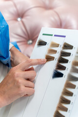 Choosing hair dye by palette. Hairdresser offers hair dye shades to client. A woman points to a...