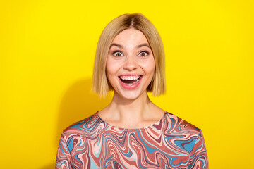 Cheerful portrait of a young woman with blonde hair wearing a colorful top against a vibrant yellow...