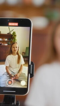 Girl records a vertical video for her vlog using a smartphone on a tripod. She waves to the camera and talks excitedly. Shot in vertical format, ideal for mobile-first content platforms. 4k footage