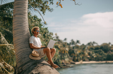 A man in shorts and sunglasses, wearing a hat, is sitting on the trunk of an old palm tree by the water