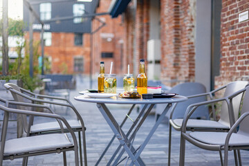 An outdoor restaurant table set for dining with drinks, snacks, and chairs, perfect for a relaxing meal in a brick-walled setting.