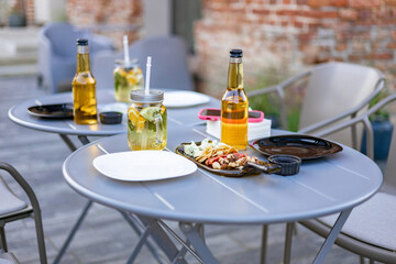 An outdoor restaurant table with drinks, food, and plates, ready for guests. No people are present.