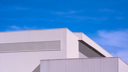 Factory industrial building in modern minimal design with geometric white aluminium corrugated metal wall and steel ventilation louver against blue sky background, low angle view