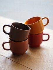 Four vibrant ceramic cups are creatively stacked on a smooth wooden table. The warm tones of the cups contrast beautifully against the natural wood evoking a cozy ambiance.
