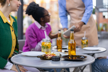 Friends enjoying drinks and snacks at an outdoor cafe, served by a waiter.