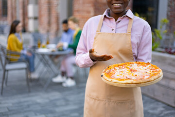 A smiling waiter presents a delicious pizza on a wooden board, ready to be served to customers...