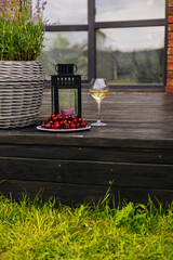 Enjoying a glass of white wine with fresh red cherries in a relaxing outdoor setting. A rustic outdoor setting showcases a glass of white wine, cherries, and a lantern on a wooden deck.