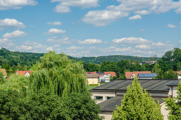 Scenic view of rooftops, green trees and distant hills under blue summer sky. High quality photo