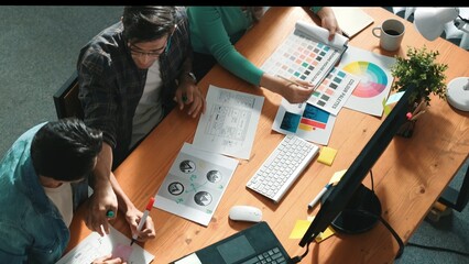 Top view of manager writing idea while team standing and giving comment. Professional designer design logo while looking at color palette and writing idea down in paper with color marker. Symposium. © InfiniteFlow