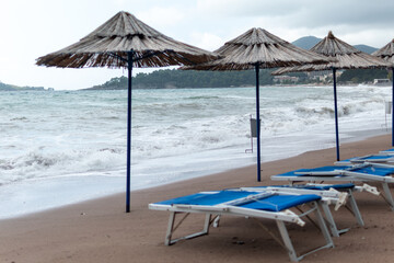 Stormy beach scene with several straw umbrellas and empty blue lounge chairs on sand with large...