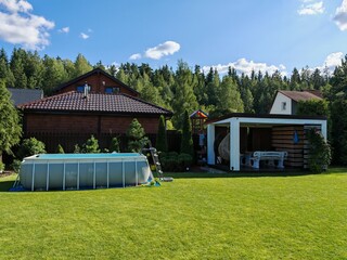 A gray rectangular frame pool made of PVC material stands on a grassy lawn near a wooden gazebo...