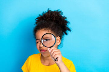 Young girl with curly hair exploring with a magnifying glass against a vibrant blue background