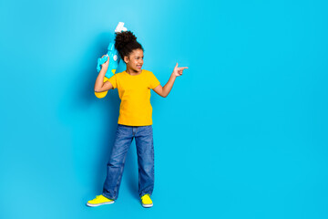 Happy girl in a yellow t-shirt posing with a water gun on blue background showcasing childhood enthusiasm and play