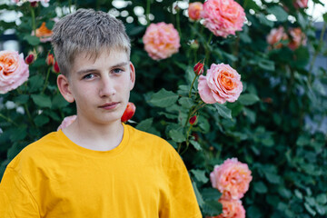 Teenage boy with VR headset, standing with hands raised in rose-filled garden. Engaged expression,...