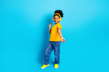Cheerful young girl wearing yellow headphones dancing in colorful casual attire against a vibrant...