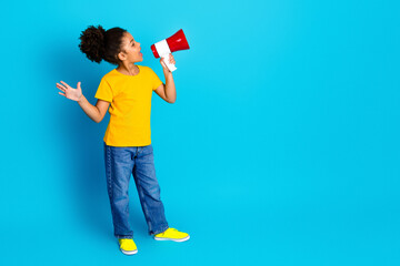 Joyful young girl with a megaphone in front of a blue background, expressing happiness and...