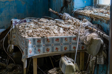 Destroyed table in an abandoned house, covered with debris and dust – floral tablecloth, old...