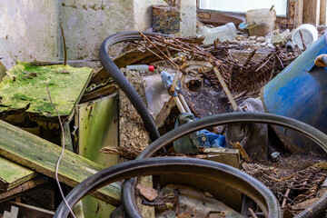 Abandoned interior filled with tangled hoses, rusty tools, broken furniture, and scattered debris,...