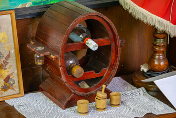 Decorative barrel-shaped bottle rack with shot glasses and a carafe, placed on a lace doily –...